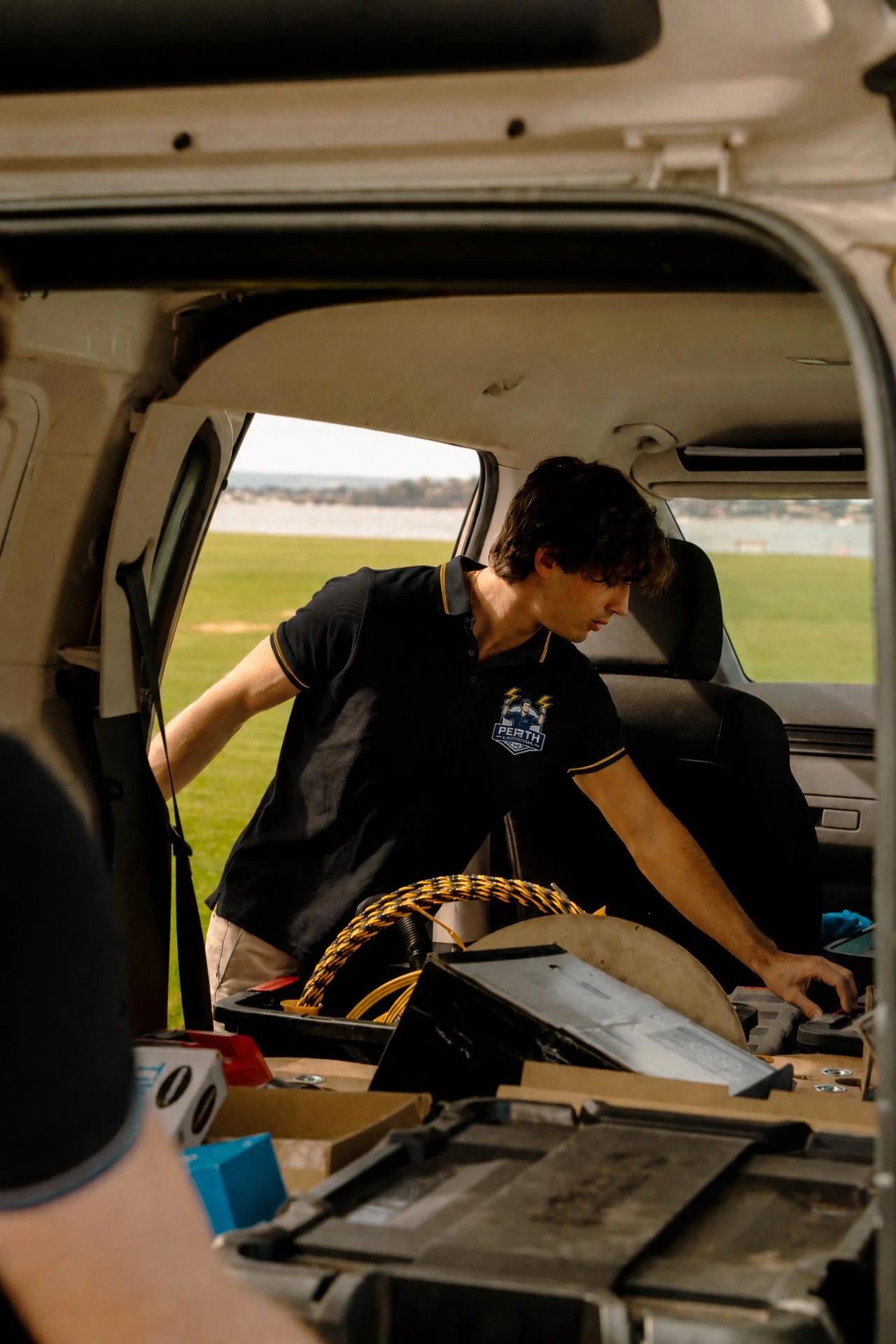 Electrician Perth technician collecting equipment from the work van in a branded polo
